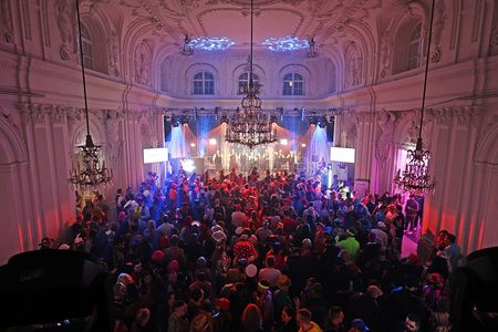Menschen feiern verkleidet in einem festlichen Saal, der blau und lila beleuchtet ist.