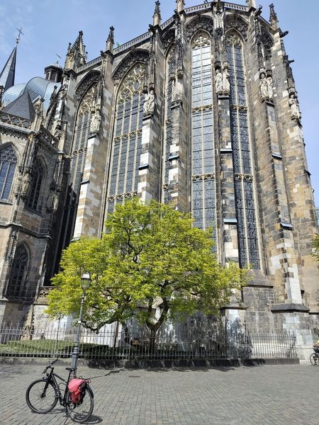 Vor der Chorhalle des Aachener Doms ist vor einem grünen Baum ein Fahrrad abgestellt.