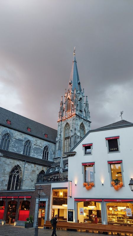 Ein grauer Kirchturm erhebt sich vor Dämmerungshimmel hinter der Bäckerei Nobis.