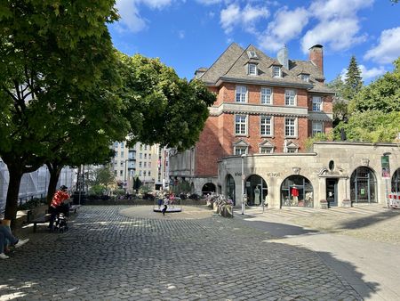 Großer Platz auf dem Burtscheider Markt mit einem Spielgerät für Kinder, Häusern und Bäumen ringsherum.