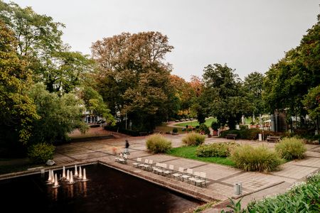 Gepflasterter kleiner Park mit einem Teich zwischen grünen Bäumen.