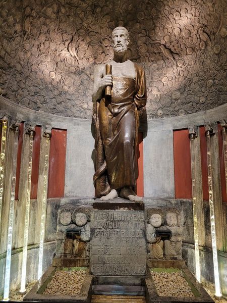 Statue eines Mannes auf einem Sockel mit einem Stab in der Hand.