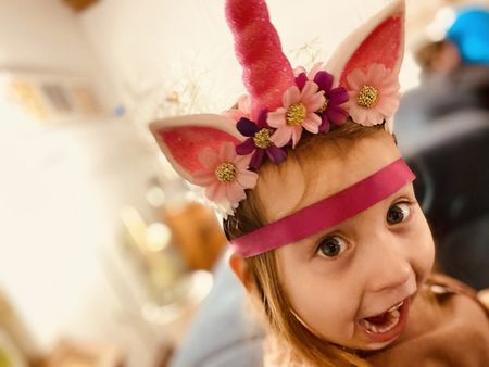 Ein kleines Mädchen mit Einhorn-Krone lacht mit weit aufgerissenem Mund.
