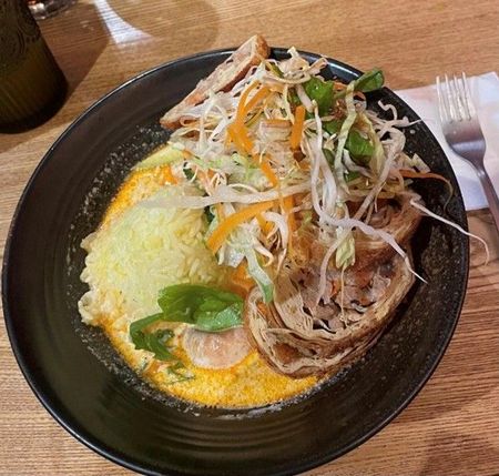 In einem schwarzen, tiefen Teller befindet sich ein asiatisches Gericht mit verschiedenem Gemüse in einer Suppe.