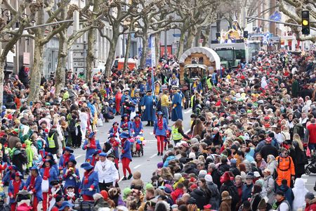 Musizierender Karnevalszug marschiert auf der Straße mit vielen unterschiedlich verkleideten Menschen an den Straßenseiten.