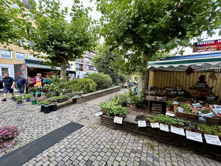 Blumenverkauf des Wochenmarktes zwischen Bäumen auf einem gepflasterten Platz..