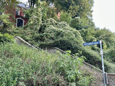 Treppenstufen führen zwischen grünen Bäumen hinauf zu einer Kirche. Am Fuße der Stufen steht ein Straßenschild, auf dem "Michaelstreppe" steht.
