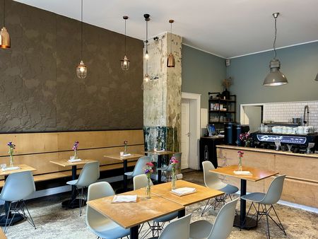 Innenraum eines Cafés mit mehreren Sitzgruppen, herabhängenden Deckenleuchten und einer Theke.