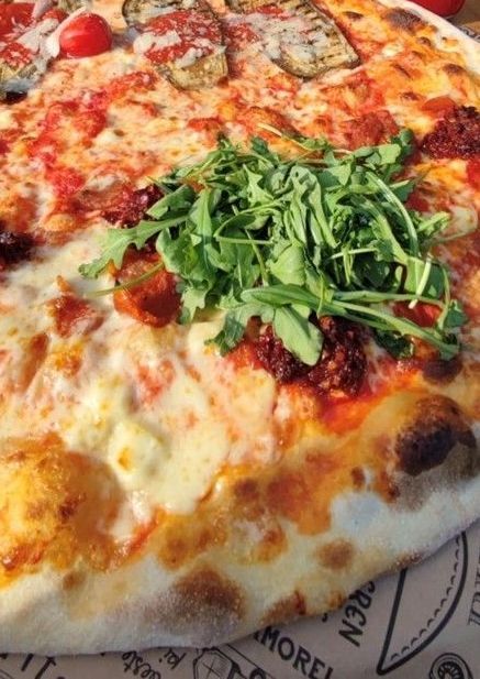 Eine große runde Pizza ist mit verschiedenem Gemüse und Rucola belegt.