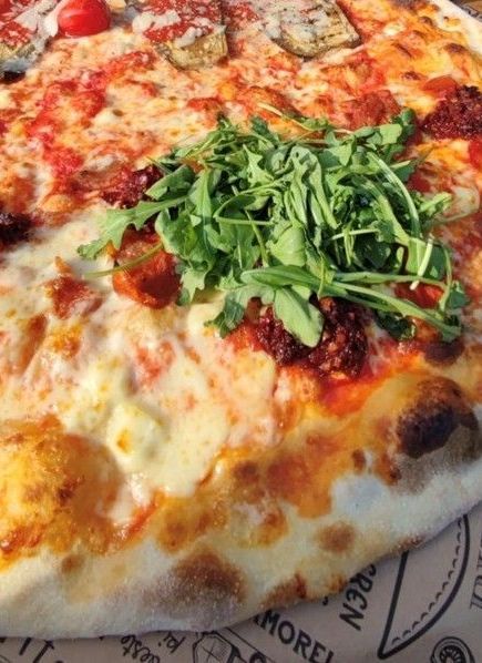 Eine große runde Pizza ist mit verschiedenem Gemüse und Rucola belegt.