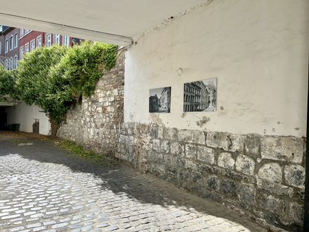 Eckiger Toreingang mit Bildern an der Wand und einem gepflastertem Weg.